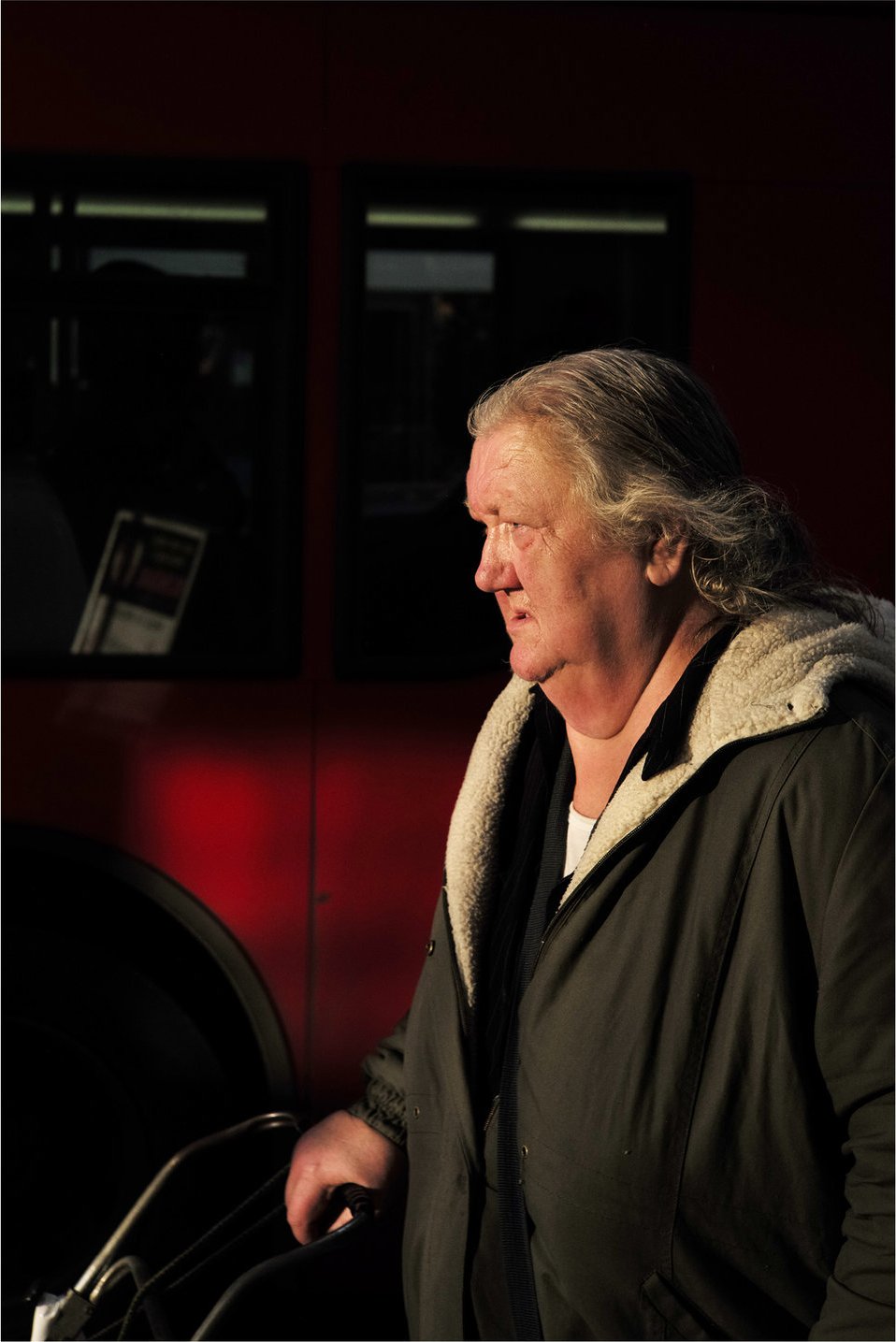 Silver-haired man waiting beside a red London bus