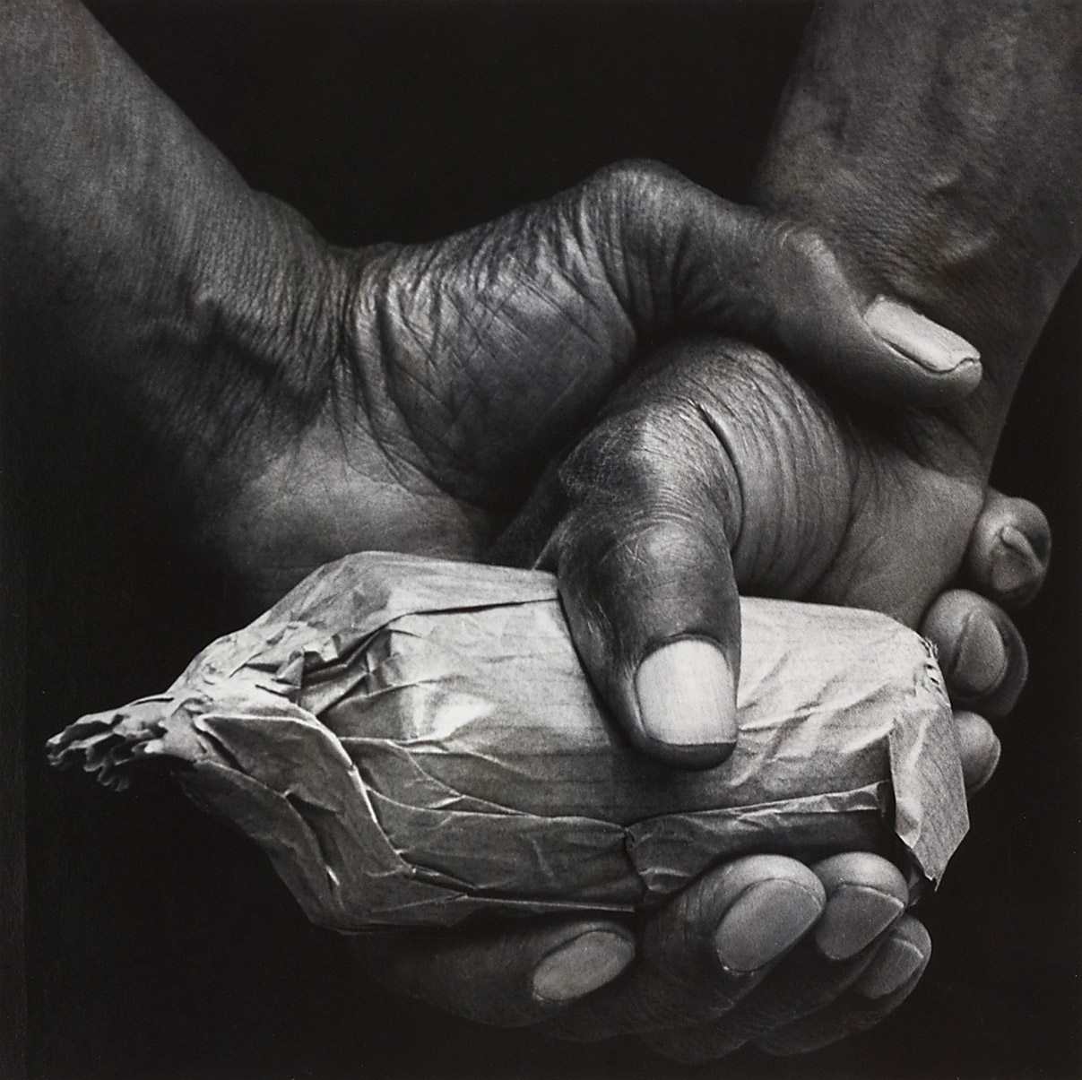 Weathered hands clasped around a small paper-wrapped parcel — photograph by Dave Heath